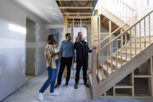 woman and two men standing at the bottom of stairs in a home under construction.